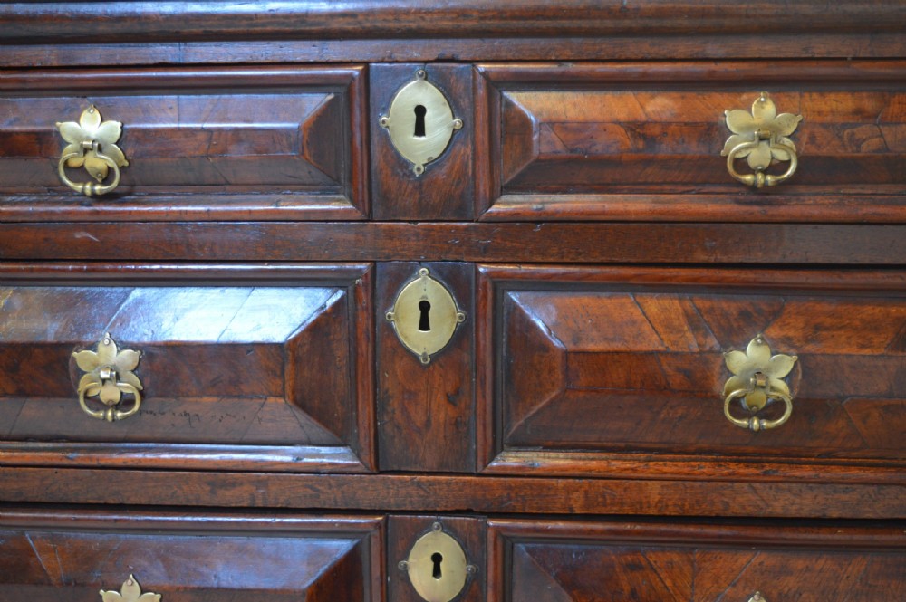 A 17th-century walnut chest of drawers with four moulded drawer fronts, brass drop handles, brass keyhole escutcheons, and large turned bun feet. View VIII