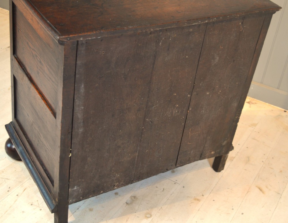 A 17th-century walnut chest of drawers with four moulded drawer fronts, brass drop handles, brass keyhole escutcheons, and large turned bun feet. View IX
