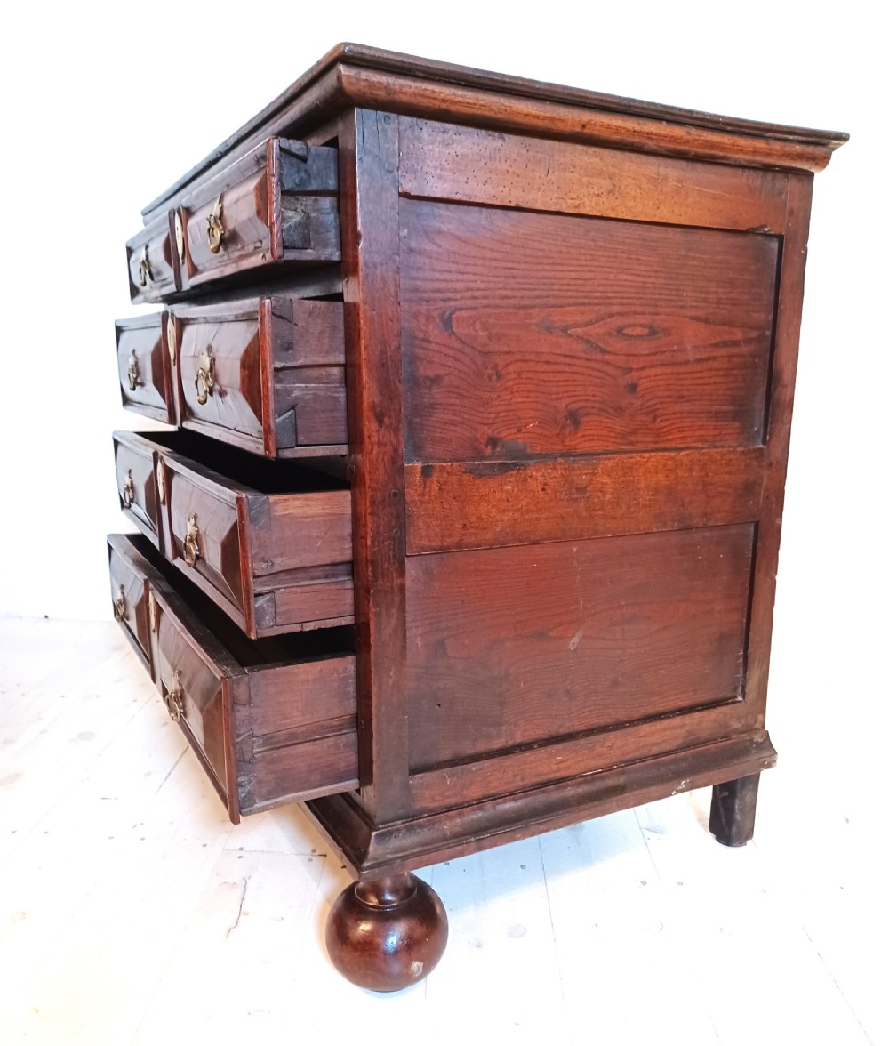 A 17th-century walnut chest of drawers with four moulded drawer fronts, brass drop handles, brass keyhole escutcheons, and large turned bun feet. View X
