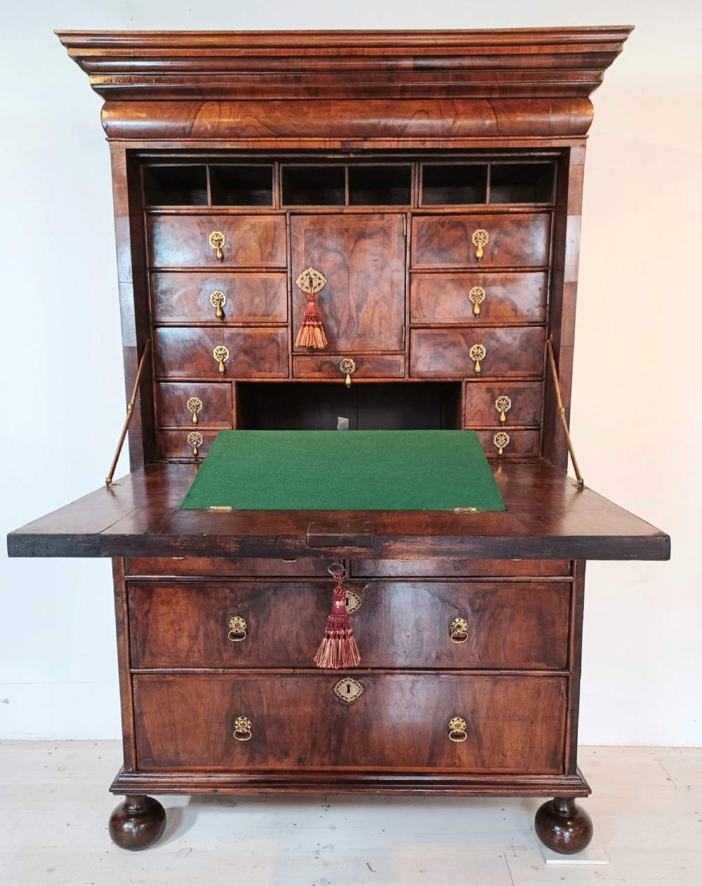 A Queen Anne walnut fall-front secretaire featuring a fitted interior with small drawers, green baize writing surface, brass drop handles, and turned bun feet.
