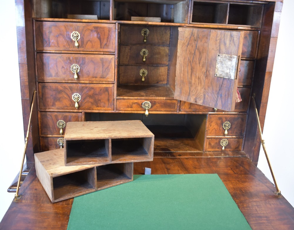 A Queen Anne walnut fall-front secretaire featuring a fitted interior with small drawers, green baize writing surface, brass drop handles, and turned bun feet. View III