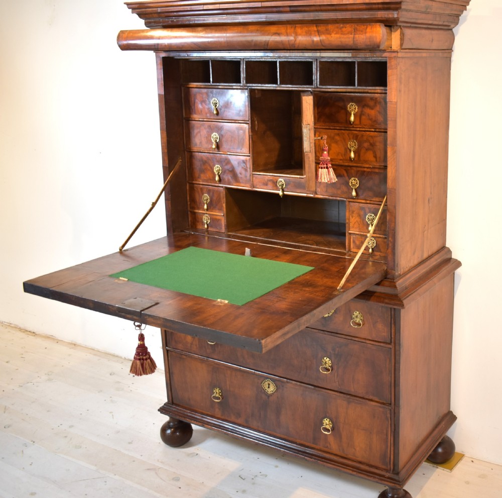 A Queen Anne walnut fall-front secretaire featuring a fitted interior with small drawers, green baize writing surface, brass drop handles, and turned bun feet. View V