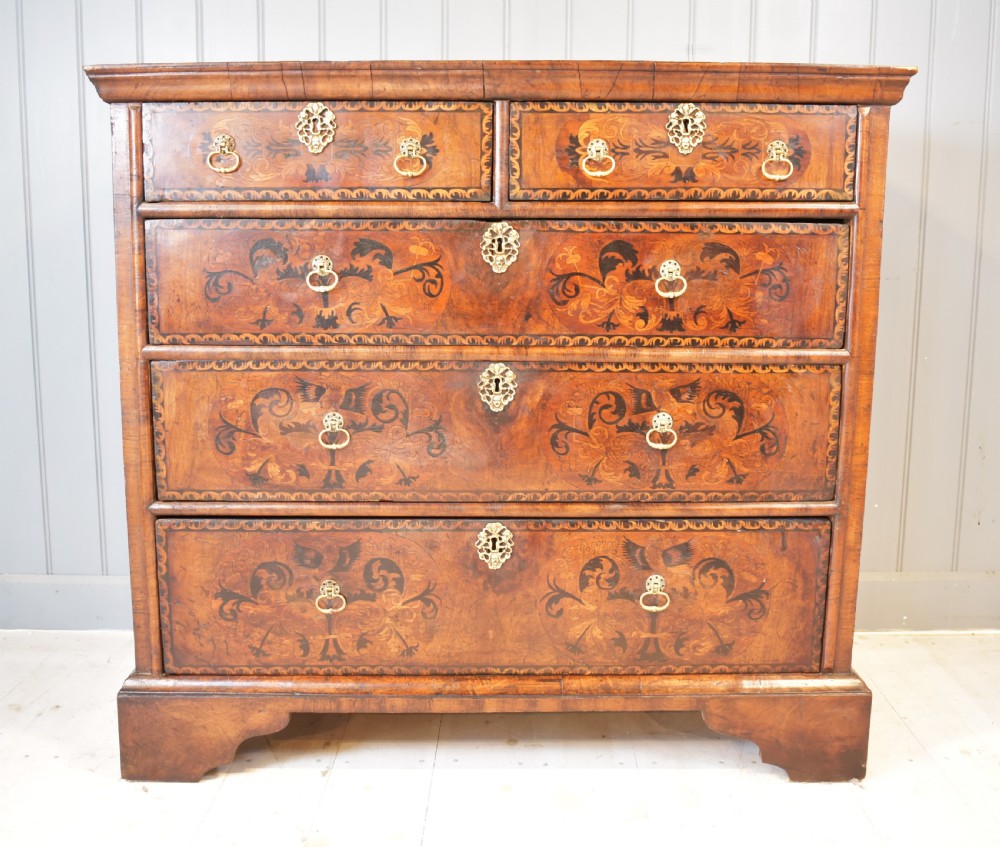 A 17th-century William and Mary walnut chest of drawers featuring intricate floral marquetry inlay, brass drop handles, decorative keyhole escutcheons, and bracket feet.