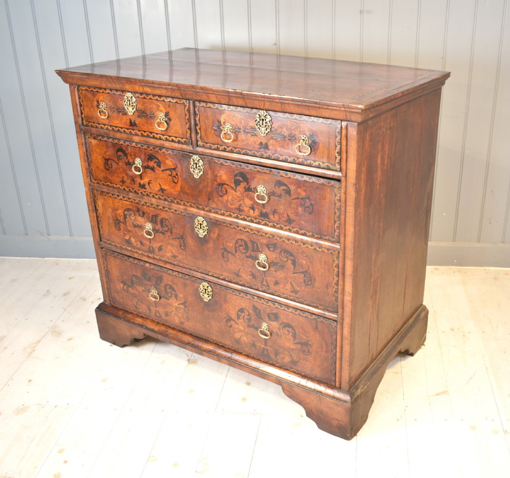A 17th-century William and Mary walnut chest of drawers featuring intricate floral marquetry inlay, brass drop handles, decorative keyhole escutcheons, and bracket feet. View II