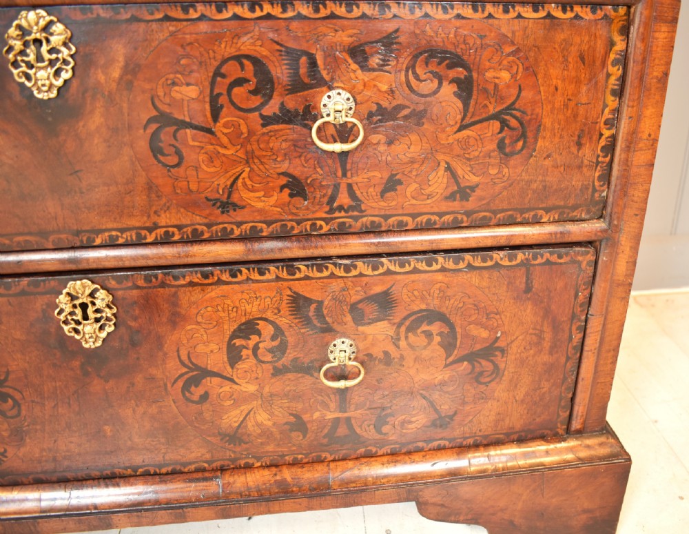 A 17th-century William and Mary walnut chest of drawers featuring intricate floral marquetry inlay, brass drop handles, decorative keyhole escutcheons, and bracket feet. View VI