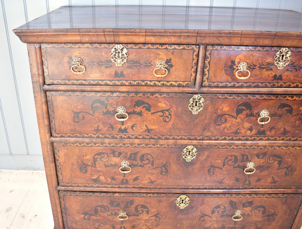 A 17th-century William and Mary walnut chest of drawers featuring intricate floral marquetry inlay, brass drop handles, decorative keyhole escutcheons, and bracket feet. View XI
