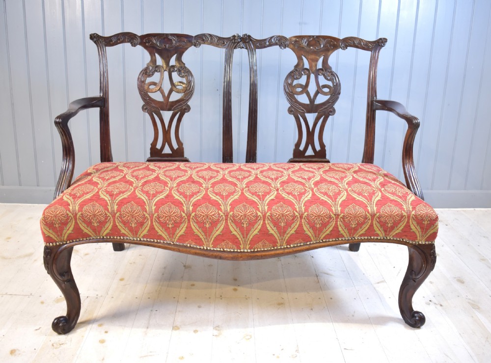 An 18th-century mahogany double-chair-back settee featuring pierced carved back splats, red patterned fabric upholstery, cabriole front legs, and curved armrests. View II