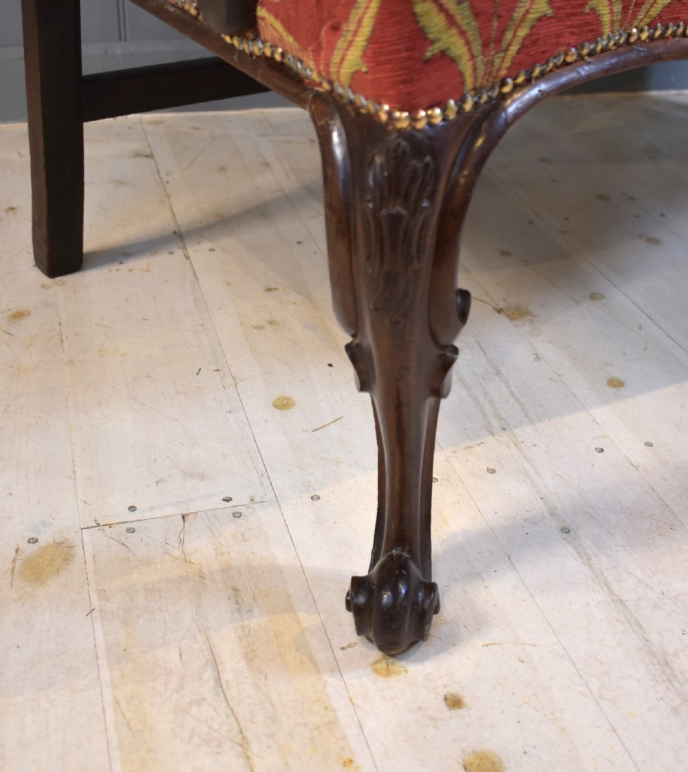 An 18th-century mahogany double-chair-back settee featuring pierced carved back splats, red patterned fabric upholstery, cabriole front legs, and curved armrests. View V