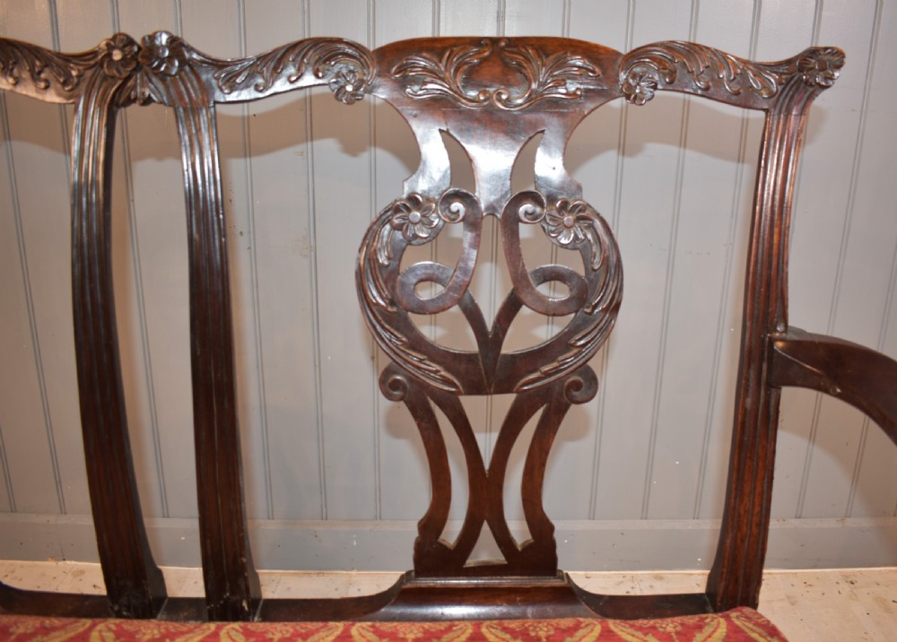 An 18th-century mahogany double-chair-back settee featuring pierced carved back splats, red patterned fabric upholstery, cabriole front legs, and curved armrests. View VII
