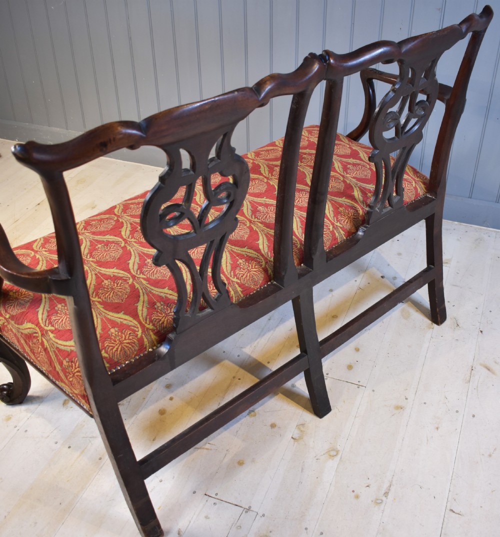 An 18th-century mahogany double-chair-back settee featuring pierced carved back splats, red patterned fabric upholstery, cabriole front legs, and curved armrests. View X