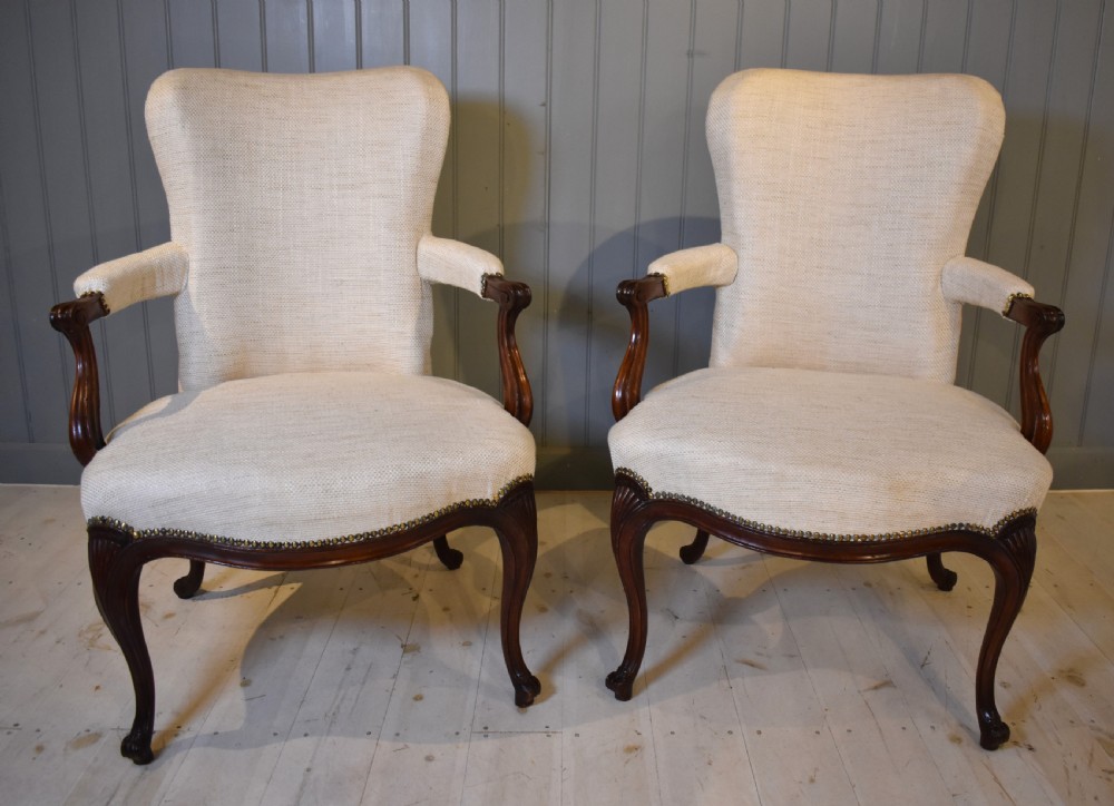 A pair of French Hepplewhite style armchairs upholstered in textured cream linen with carved dark mahogany frames and brass stud detailing.