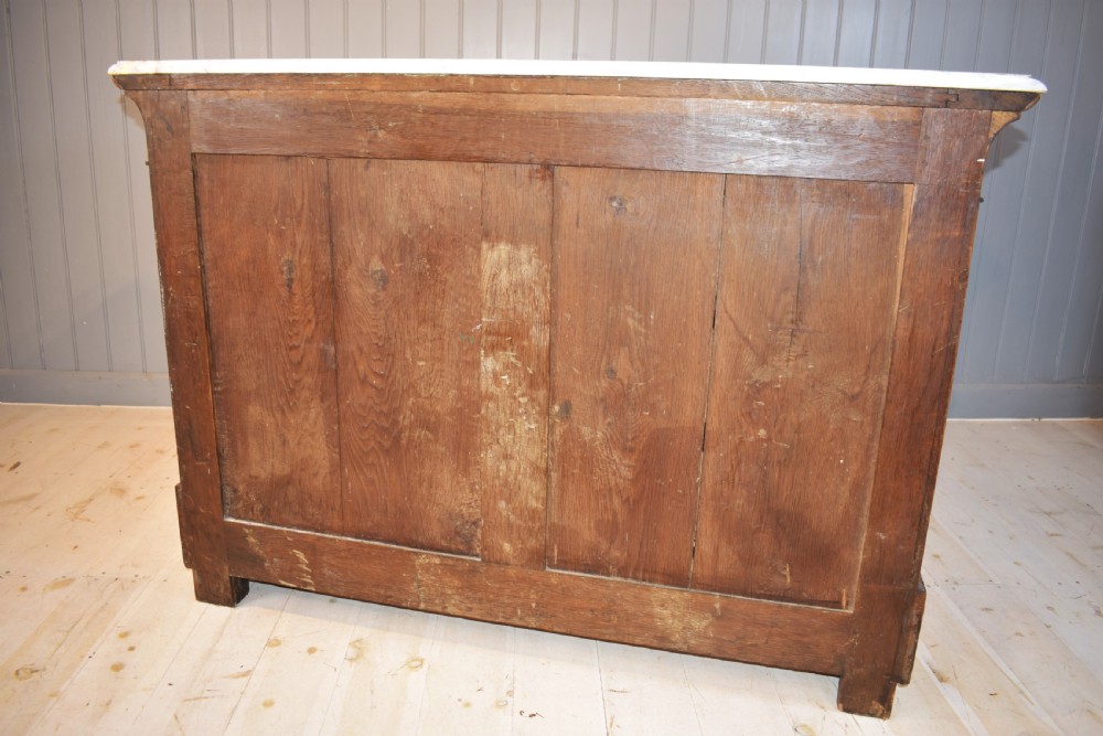 A 19th-century French Empire flame mahogany commode featuring a white marble top, three large drawers with gilt-bronze wreath handles, and flanking columns topped with ormolu accents. View XVII