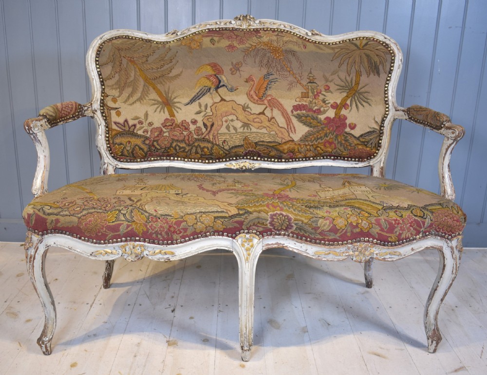 A French Louis XV style painted wooden settee with serpentine rails, cabriole legs, and woven tapestry upholstery featuring birds and palm trees. View II