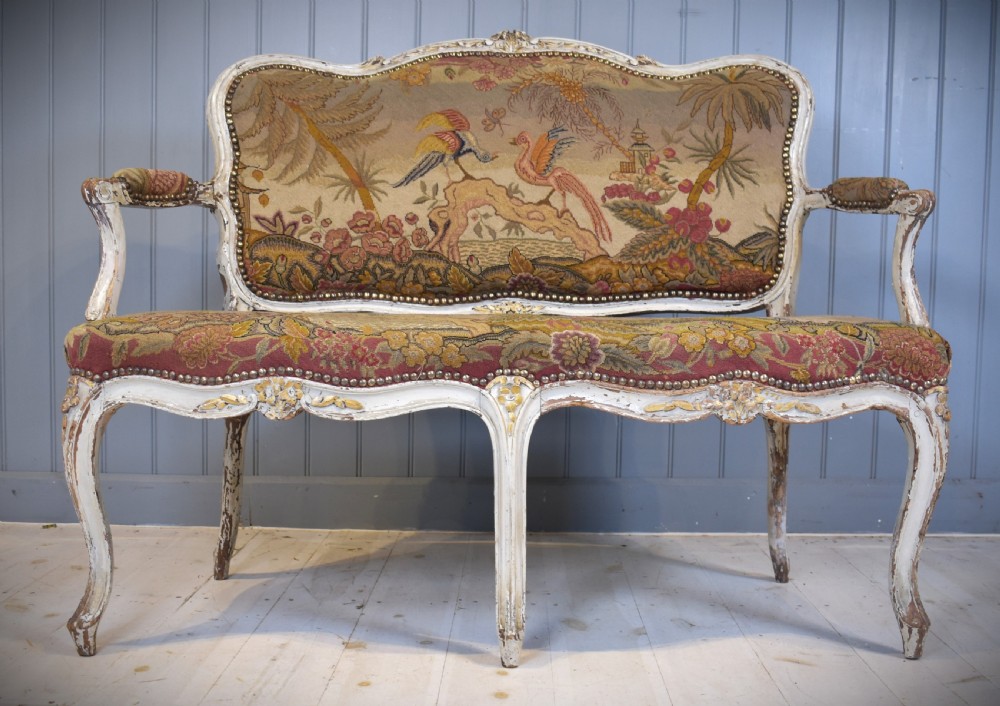 A French Louis XV style painted wooden settee with serpentine rails, cabriole legs, and woven tapestry upholstery featuring birds and palm trees. View III