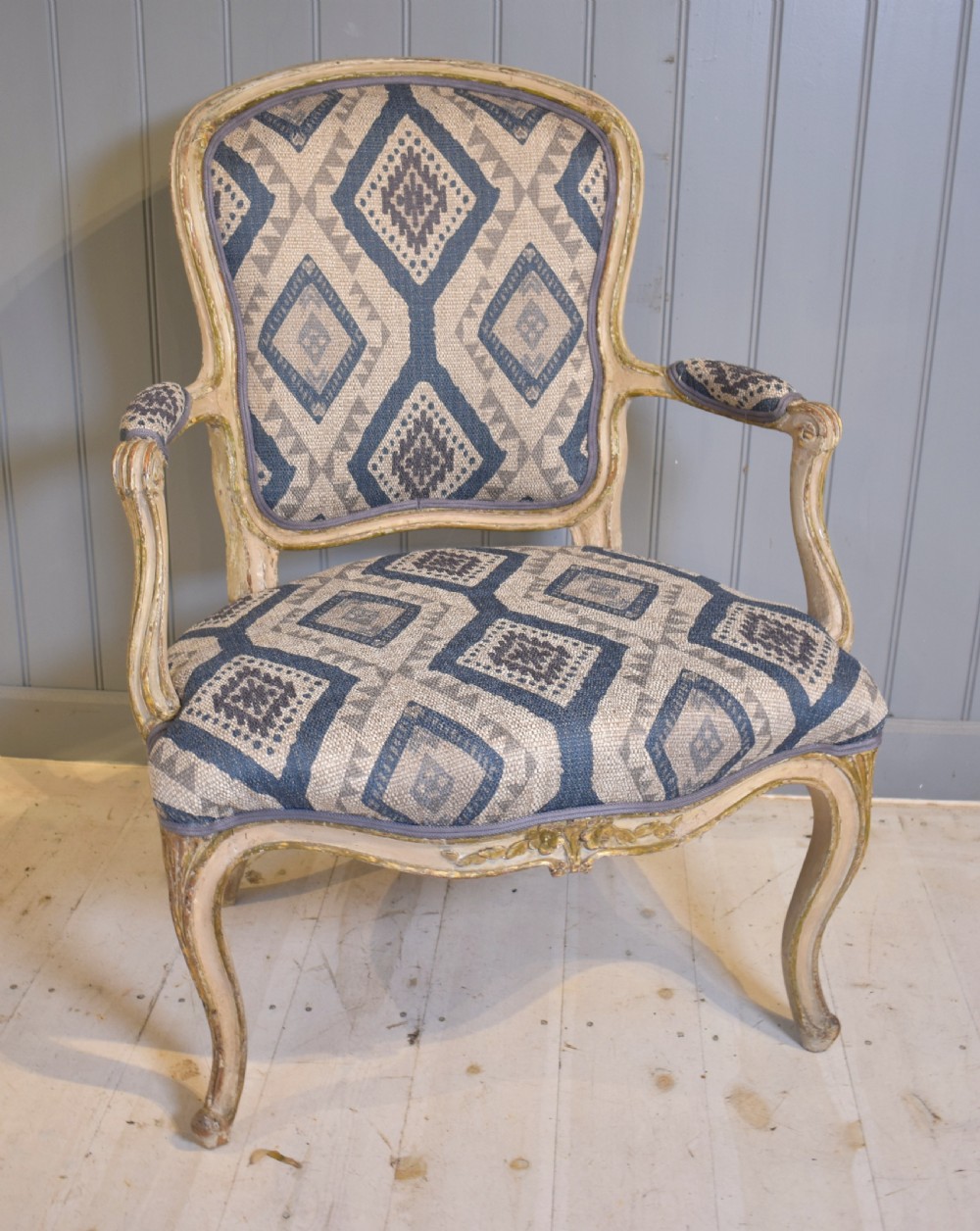 A French painted fauteuil armchair featuring cabriole legs, a carved cream frame with distressed finish, and blue geometric upholstery.