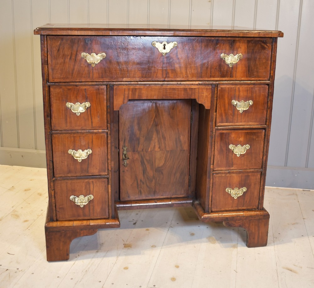 An early 18th-century George I walnut kneehole desk featuring brass handles, a central recessed cupboard, and bracket feet.