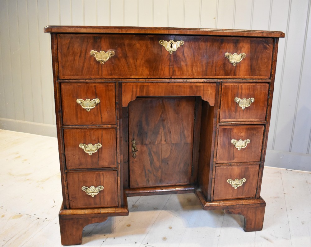 An early 18th-century George I walnut kneehole desk featuring brass handles, a central recessed cupboard, and bracket feet. View II