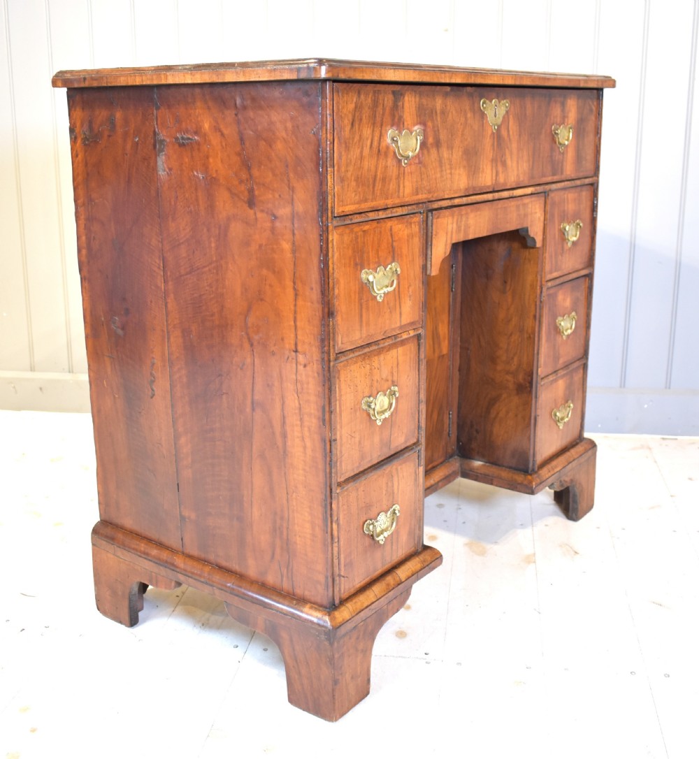 An early 18th-century George I walnut kneehole desk featuring brass handles, a central recessed cupboard, and bracket feet. View V