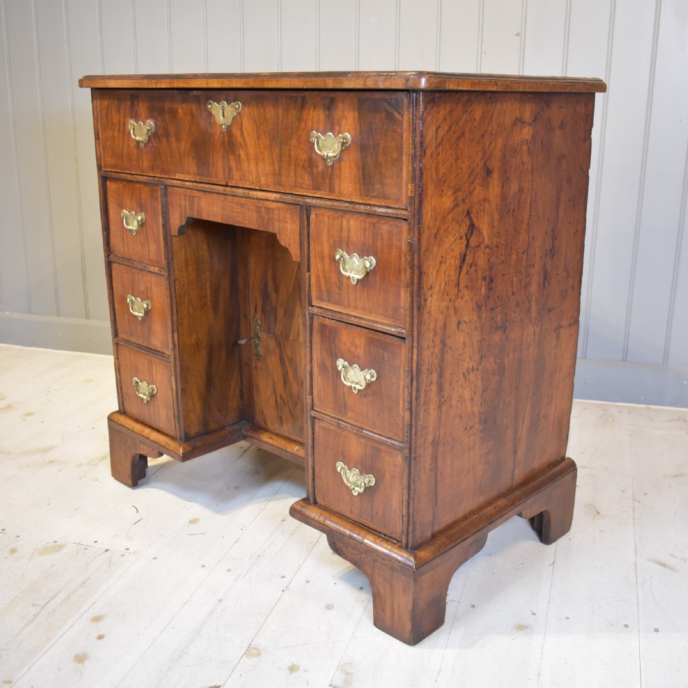 An early 18th-century George I walnut kneehole desk featuring brass handles, a central recessed cupboard, and bracket feet. View VI