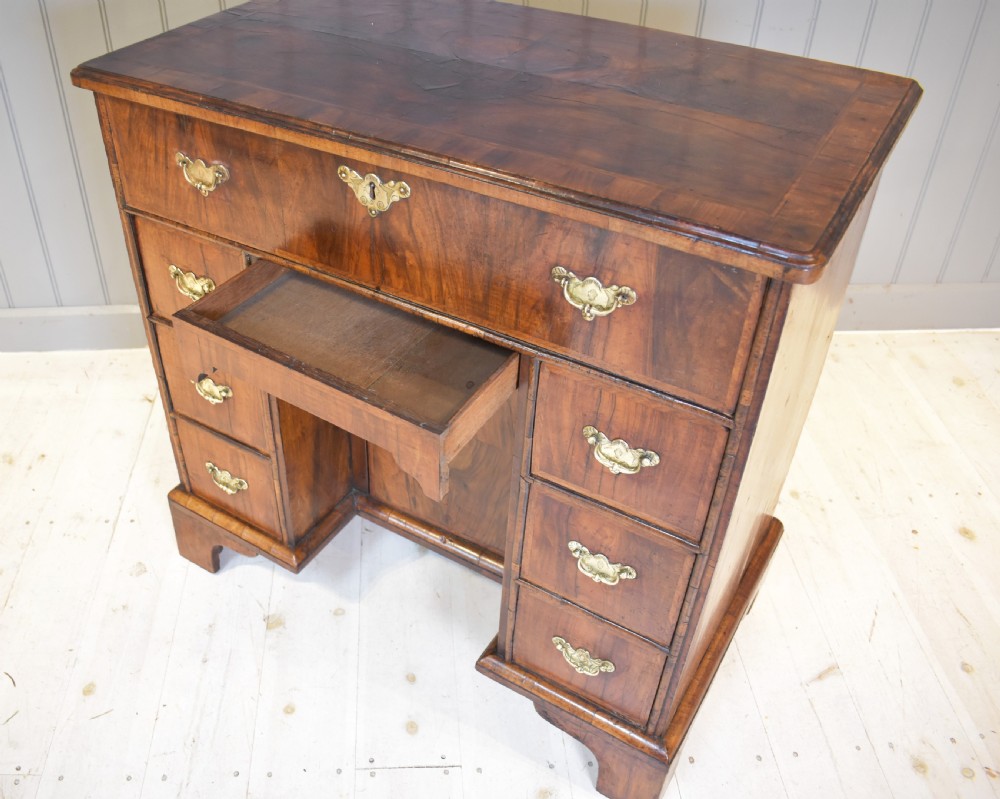 An early 18th-century George I walnut kneehole desk featuring brass handles, a central recessed cupboard, and bracket feet. View XI
