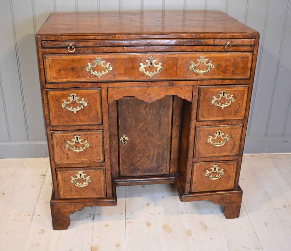 An antique Georgian style kneehole desk in burr walnut and burr oak veneers featuring brass handles, a central recessed cupboard, and drawers supported by bracket feet.