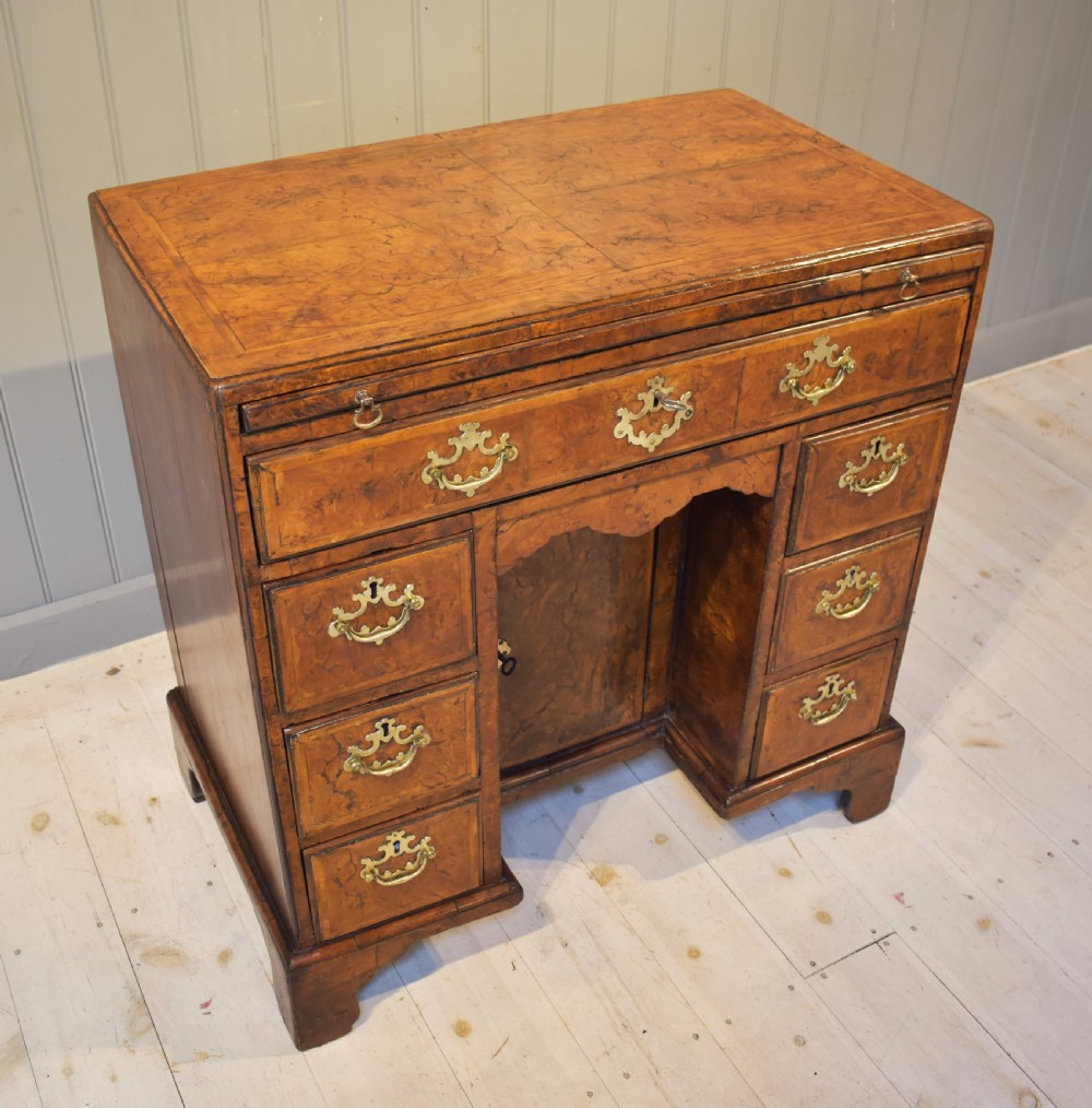 An antique Georgian style kneehole desk in burr walnut and burr oak veneers featuring brass handles, a central recessed cupboard, and drawers supported by bracket feet. View II