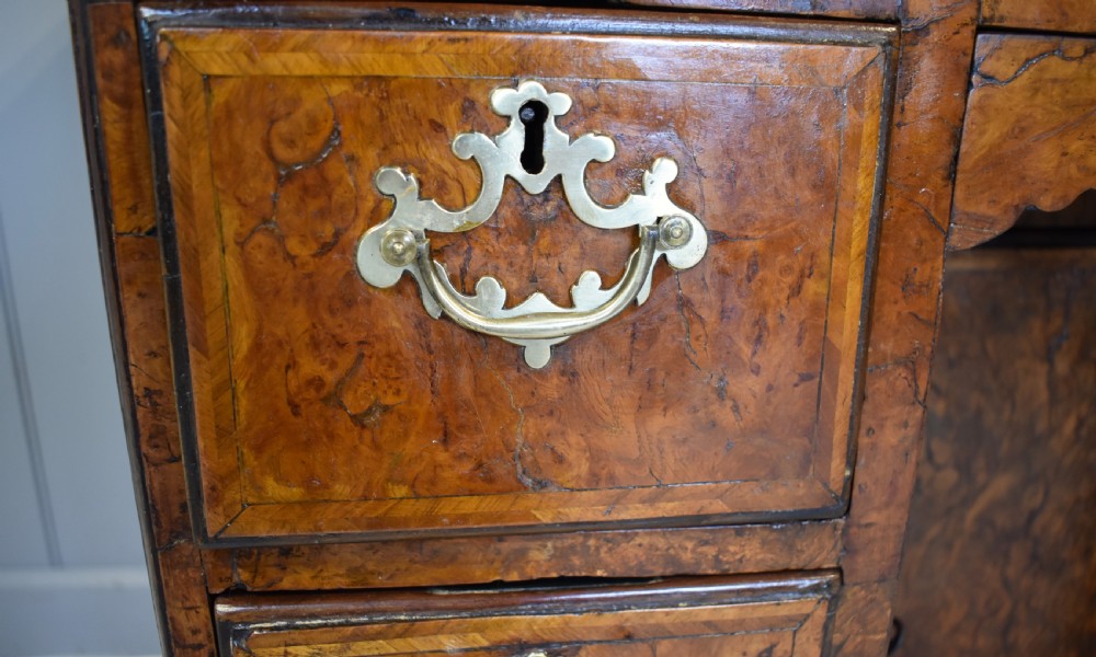 An antique Georgian style kneehole desk in burr walnut and burr oak veneers featuring brass handles, a central recessed cupboard, and drawers supported by bracket feet. View III