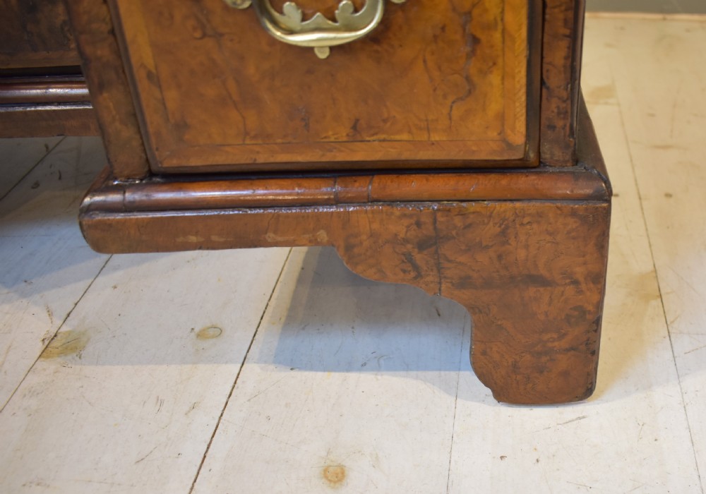 An antique Georgian style kneehole desk in burr walnut and burr oak veneers featuring brass handles, a central recessed cupboard, and drawers supported by bracket feet. View X