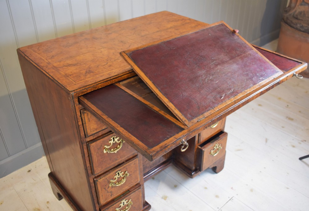 An antique Georgian style kneehole desk in burr walnut and burr oak veneers featuring brass handles, a central recessed cupboard, and drawers supported by bracket feet. View XI