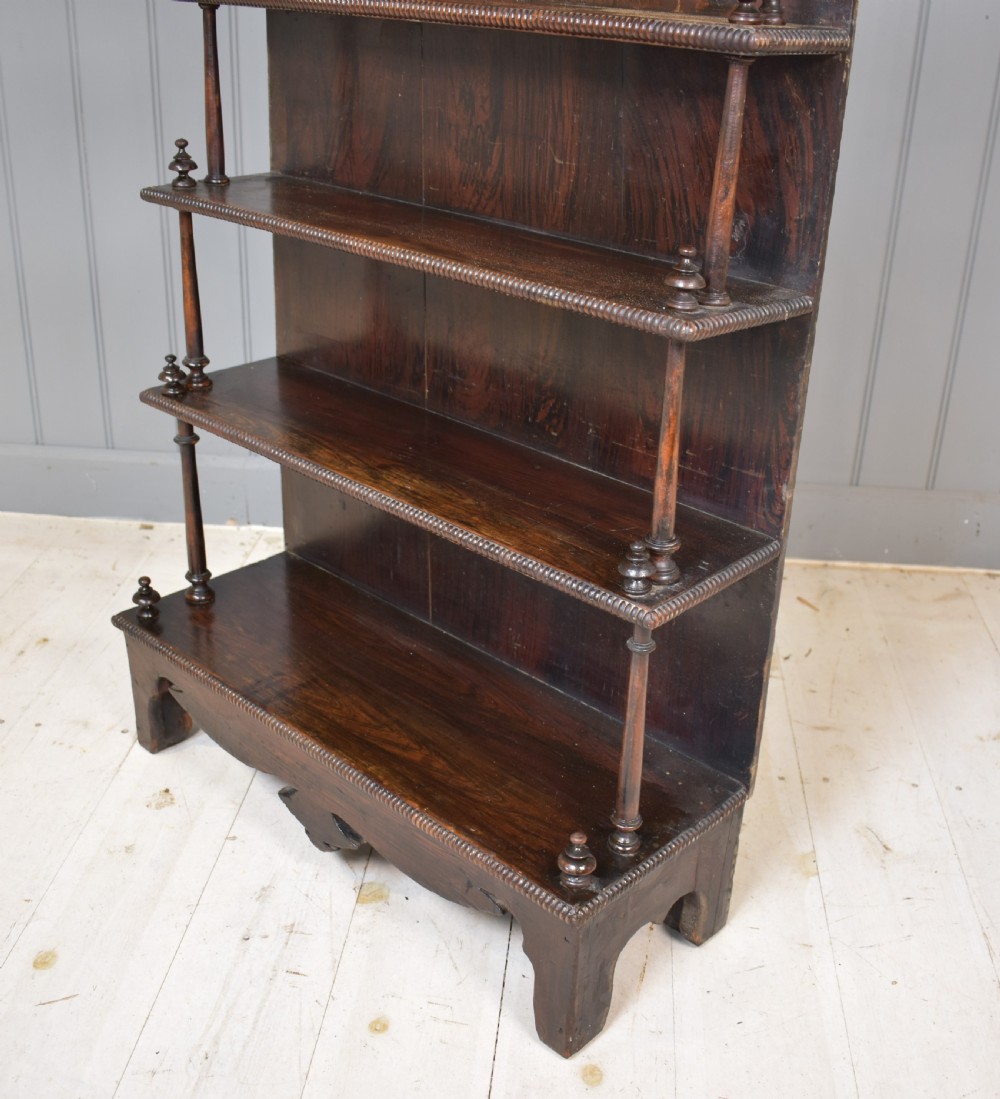An antique dark mahogany open bookcase featuring four tiered shelves, turned spindle supports, beaded edging, and a carved scrolled crest. View V