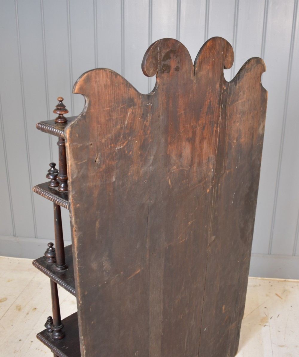 An antique dark mahogany open bookcase featuring four tiered shelves, turned spindle supports, beaded edging, and a carved scrolled crest. View VIII