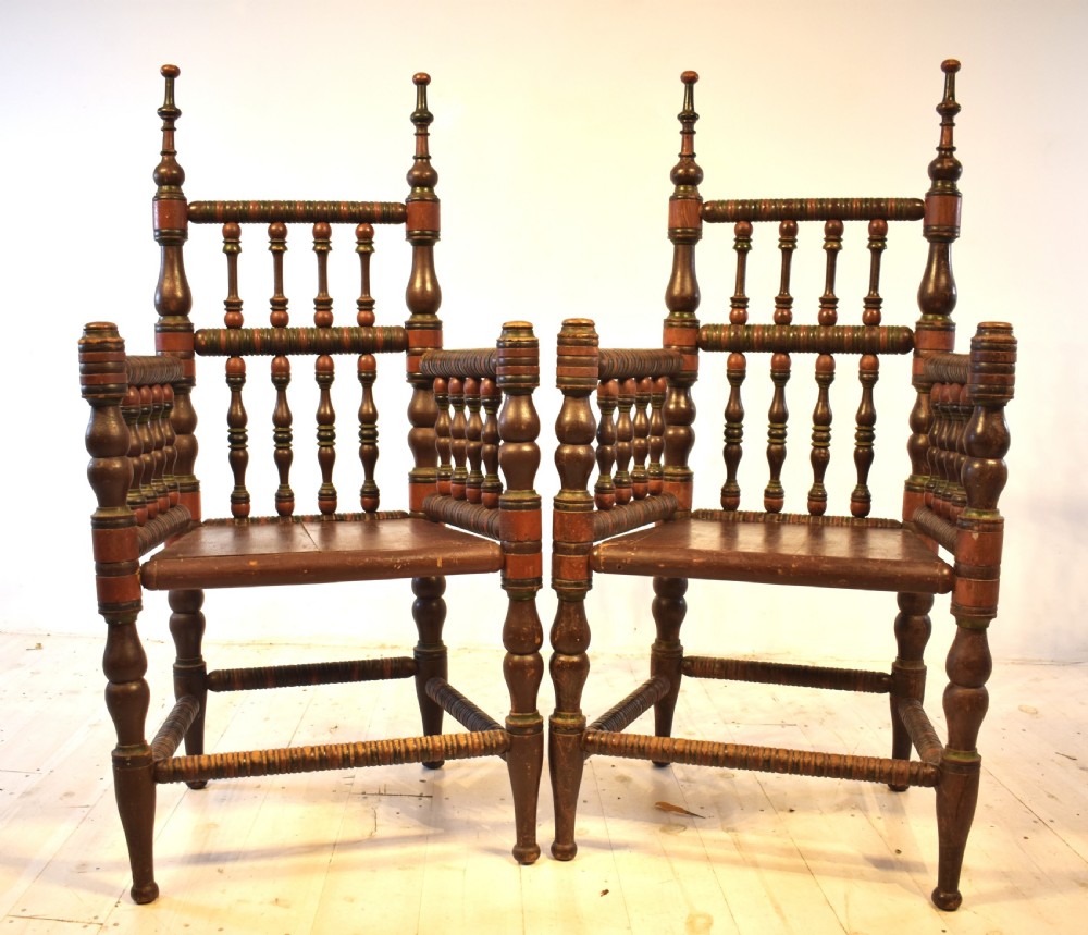 A pair of antique Swedish turned wood armchairs featuring bobbin spindles, tall finials, and dark red and brown paint details.