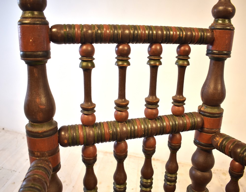 A pair of antique Swedish turned wood armchairs featuring bobbin spindles, tall finials, and dark red and brown paint details. View X