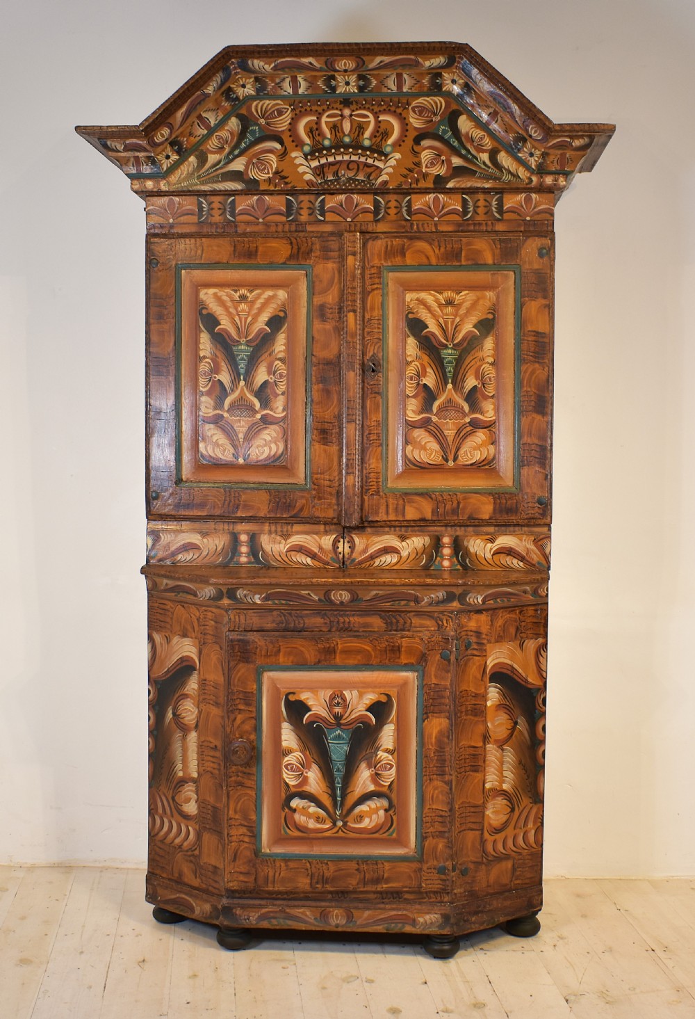 A two-tier Swedish painted pine corner cupboard decorated with hand-painted floral motifs and an arched pediment.