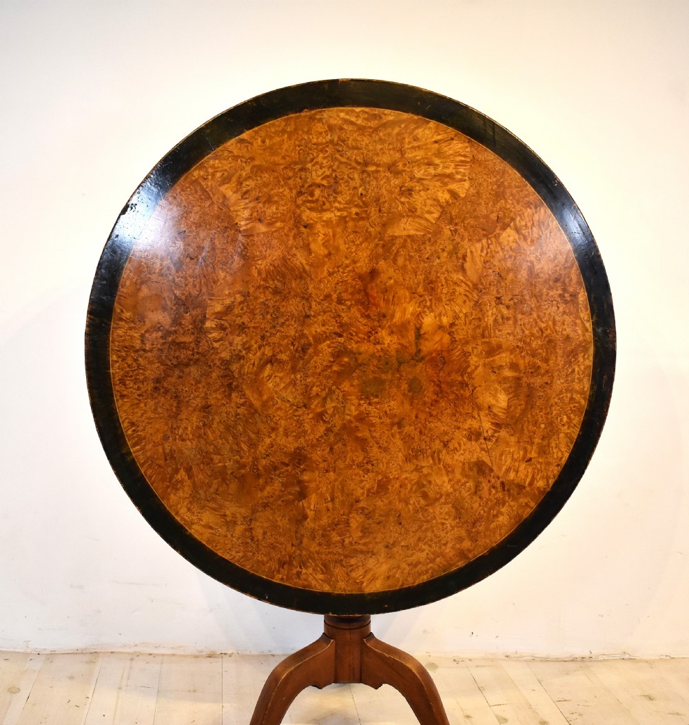 A circular burr wood tilt top table shown in its vertical position, supported by a turned central column and three cabriole legs. View II