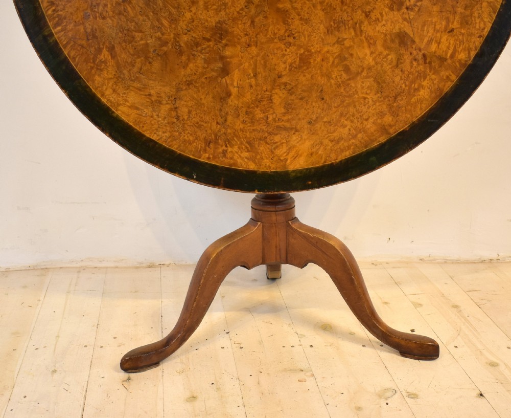 A circular burr wood tilt top table shown in its vertical position, supported by a turned central column and three cabriole legs. View III