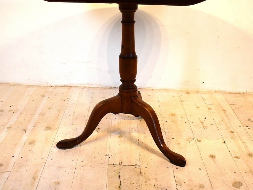 A circular burr wood tilt top table shown in its vertical position, supported by a turned central column and three cabriole legs. View IV