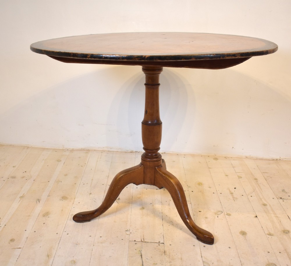 A circular burr wood tilt top table shown in its vertical position, supported by a turned central column and three cabriole legs. View V