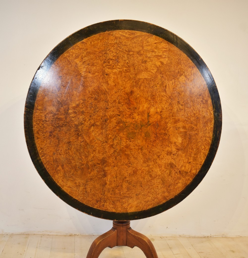 A circular burr wood tilt top table shown in its vertical position, supported by a turned central column and three cabriole legs. View VII