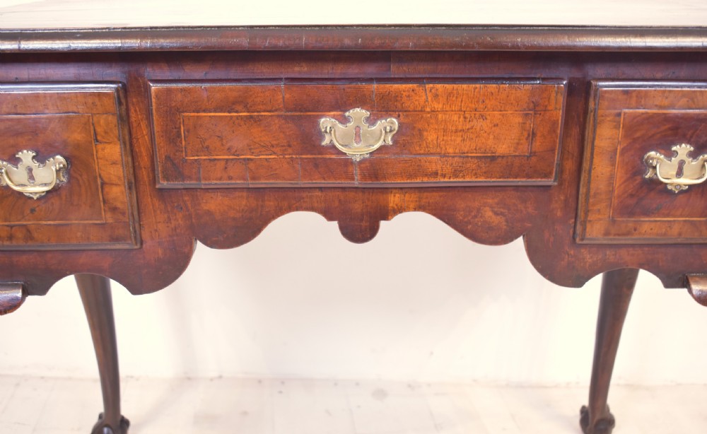 An antique Queen Anne walnut lowboy table featuring three drawers, brass handles, a shaped apron, and carved cabriole legs ending in ball and claw feet. View II
