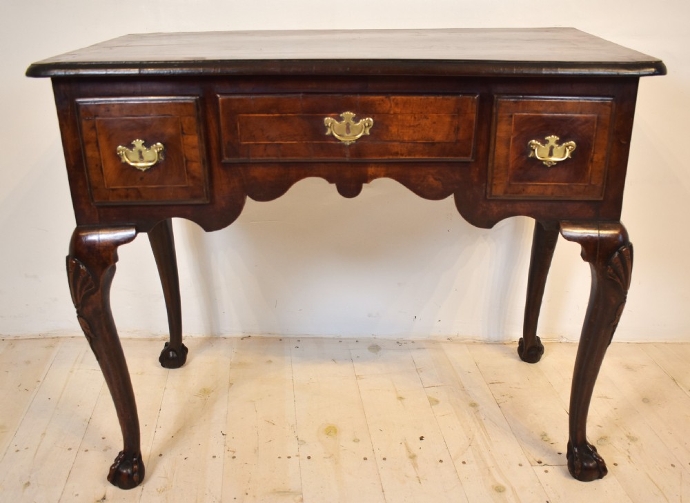 An antique Queen Anne walnut lowboy table featuring three drawers, brass handles, a shaped apron, and carved cabriole legs ending in ball and claw feet. View IV