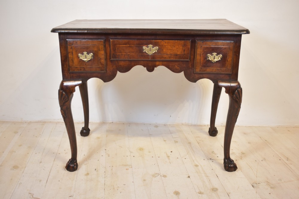 An antique Queen Anne walnut lowboy table featuring three drawers, brass handles, a shaped apron, and carved cabriole legs ending in ball and claw feet. View X
