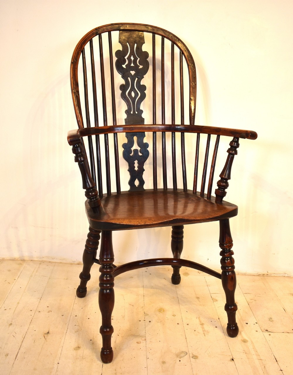 An antique yew wood Windsor armchair featuring a high hoop back with a decorative pierced splat, turned spindles, a shaped saddle seat, and turned legs joined by a curved stretcher.