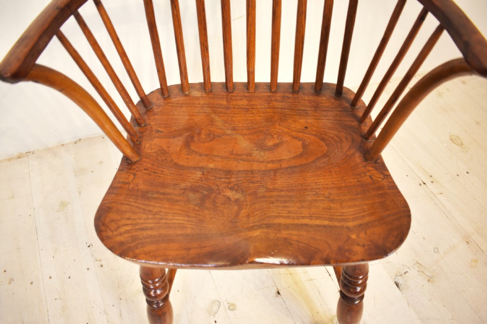 An antique wooden stick back Windsor armchair featuring a curved hoop backrest, spindle supports, a saddle seat, turned front legs, and a rich warm brown patina. View II
