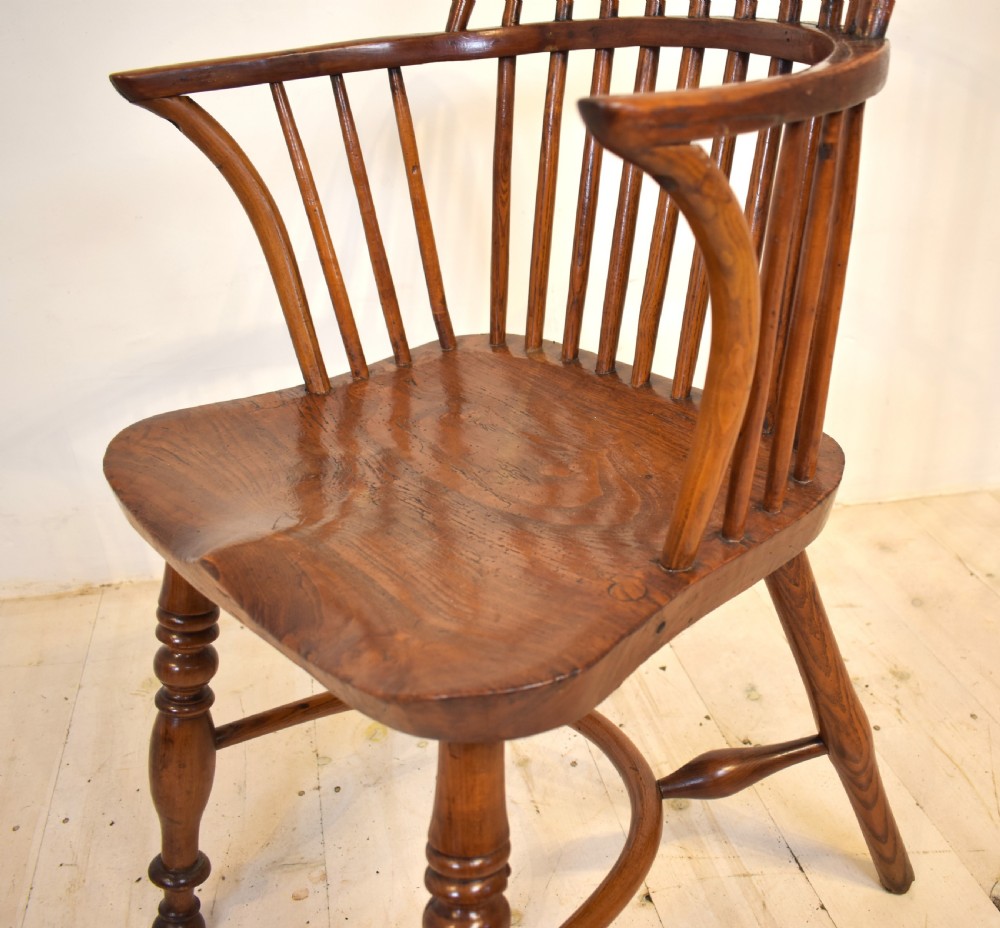 An antique wooden stick back Windsor armchair featuring a curved hoop backrest, spindle supports, a saddle seat, turned front legs, and a rich warm brown patina. View III