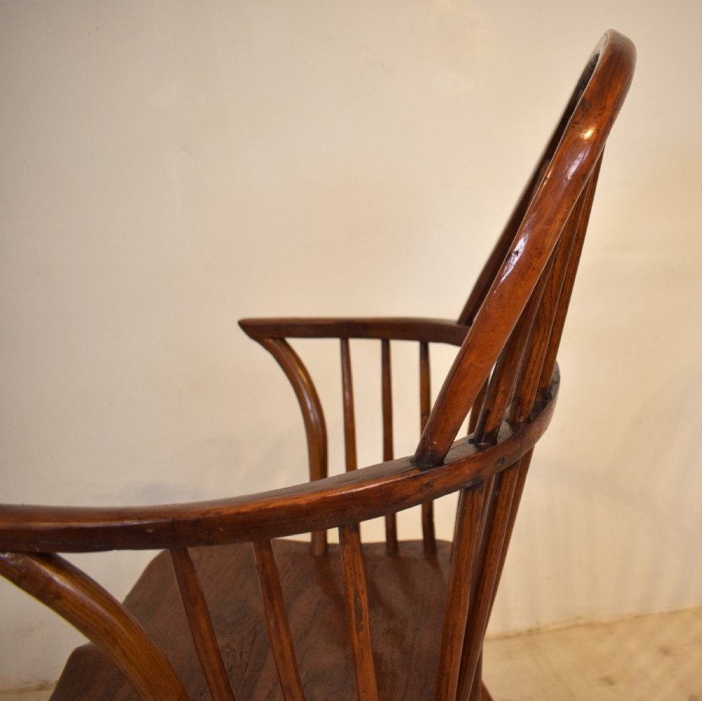 An antique wooden stick back Windsor armchair featuring a curved hoop backrest, spindle supports, a saddle seat, turned front legs, and a rich warm brown patina. View IV