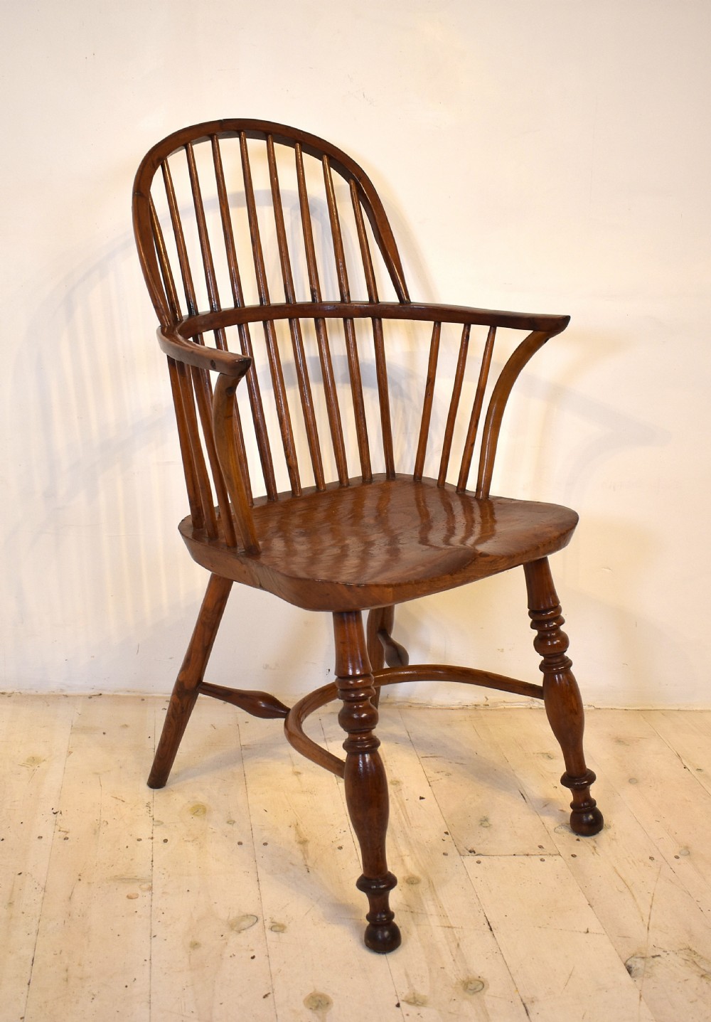 An antique wooden stick back Windsor armchair featuring a curved hoop backrest, spindle supports, a saddle seat, turned front legs, and a rich warm brown patina. View V