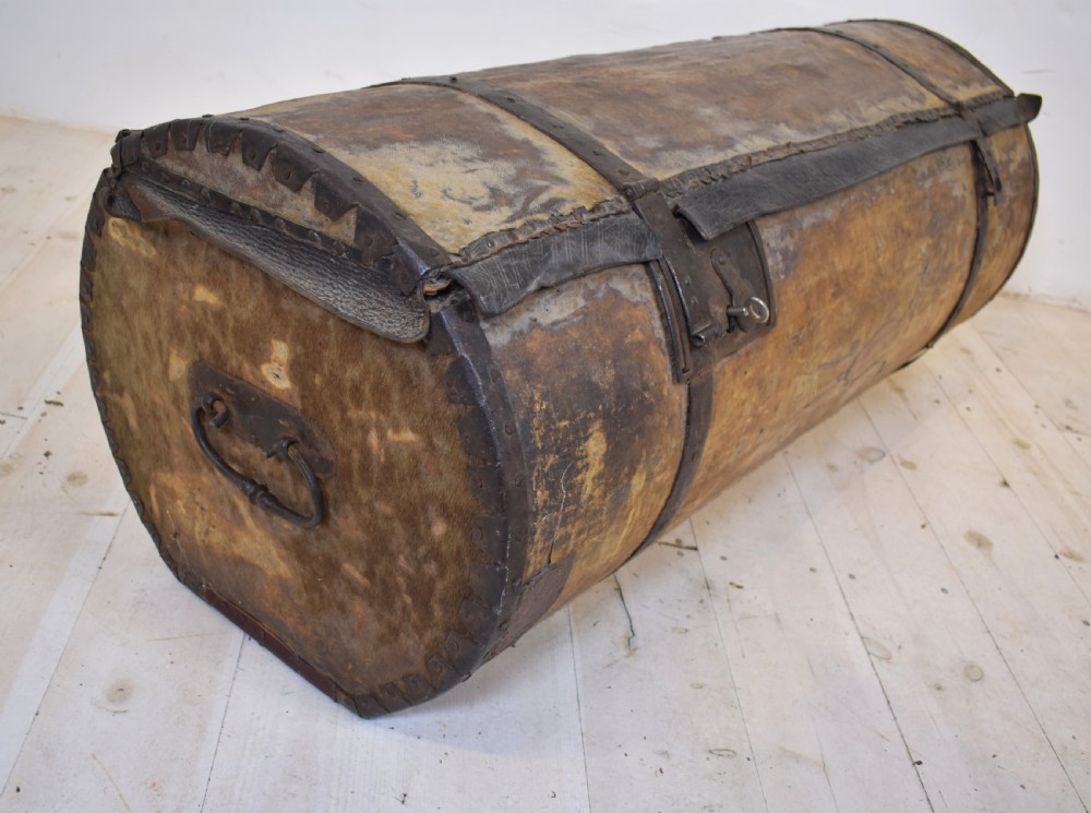 An antique cylindrical hide-covered coffer bound with dark leather trim and heavy iron bands with side handles.