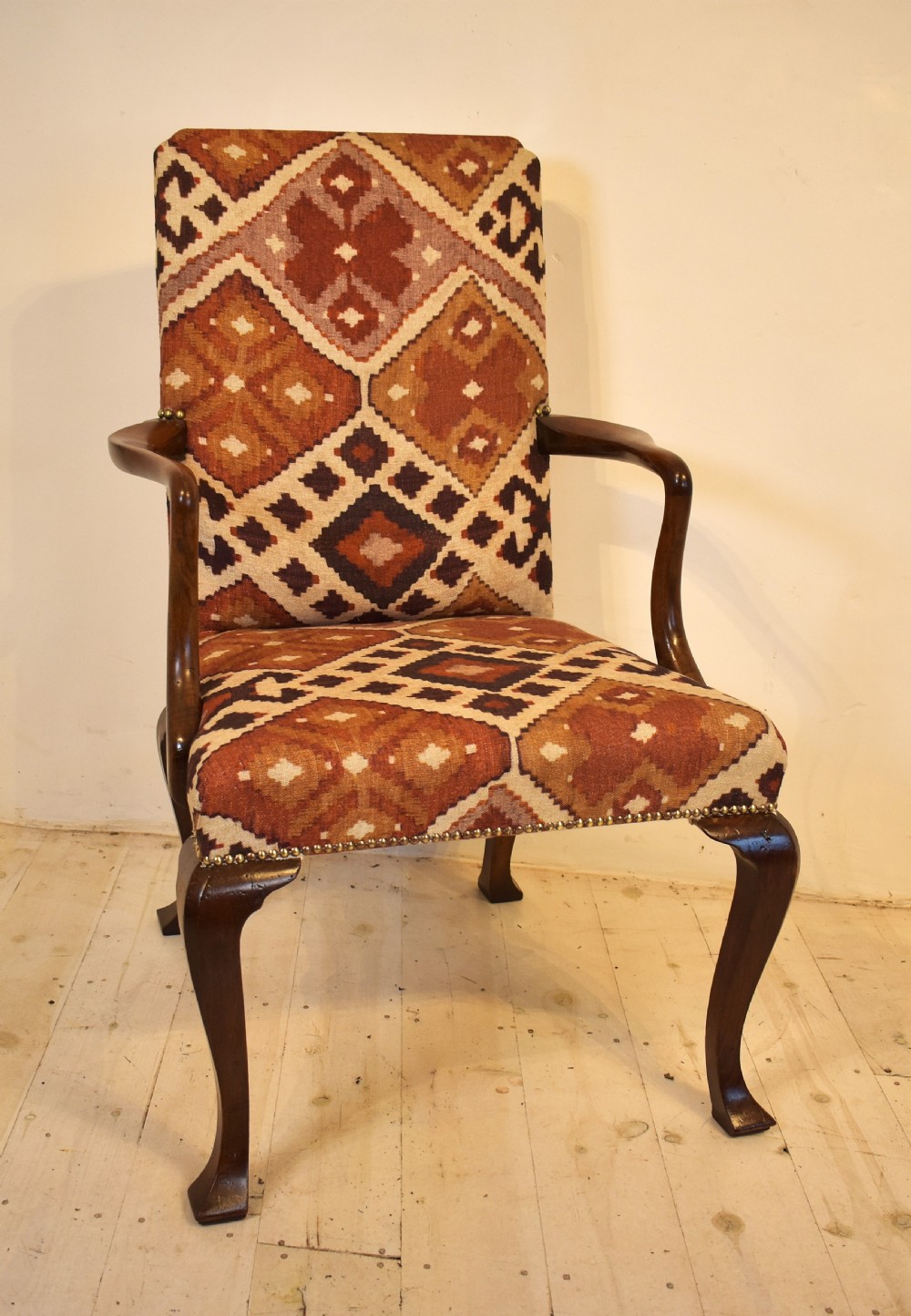 A walnut open armchair with cabriole front legs, shaped wooden arms, brass studding, and geometric terracotta tapestry upholstery.