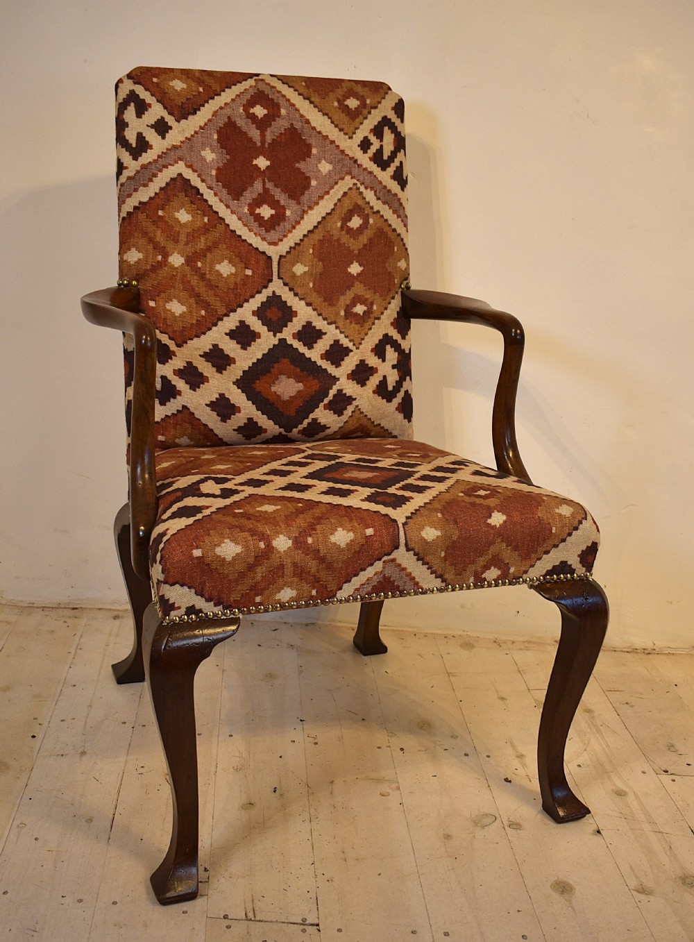 A walnut open armchair with cabriole front legs, shaped wooden arms, brass studding, and geometric terracotta tapestry upholstery. View VI
